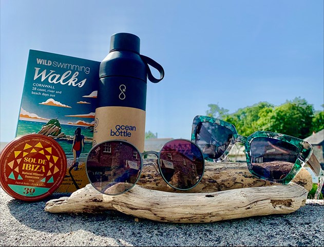 Book, water bottle and sunglasses on a beach with some driftwood